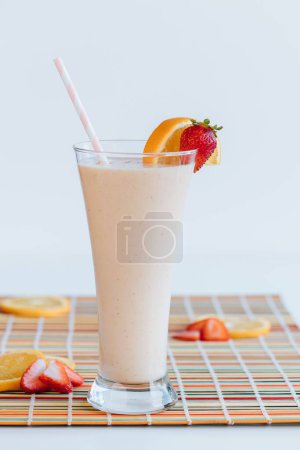 Photo for A vertical shot of a glass of milkshake with orange and strawberry on a colorful fabric with white background - Royalty Free Image
