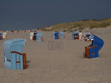Téléchargez les photos : Les chaises de plage à capuchon colorées, sur la plage de sable de l'île Juist, par une journée nuageuse, avec une colline herbeuse en arrière-plan - en image libre de droit