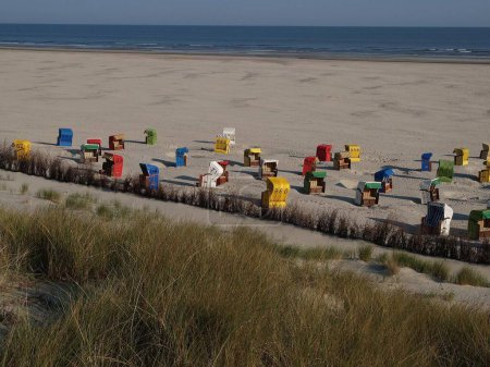 Téléchargez les photos : Une vue fascinante sur les chaises de plage à capuchon colorées sur la plage de sable, avec des vagues en arrière-plan par une journée ensoleillée sur l'île Juist dans la mer du Nord - en image libre de droit