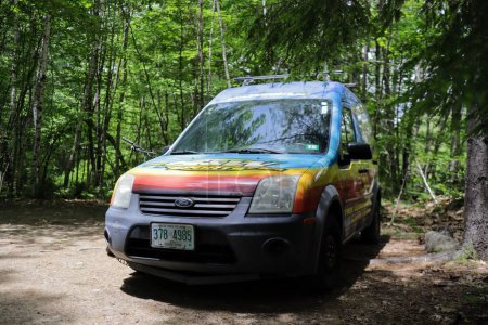 Foto de Una pequeña furgoneta Ford estacionada en un sendero en un denso bosque verde durante el día - Imagen libre de derechos