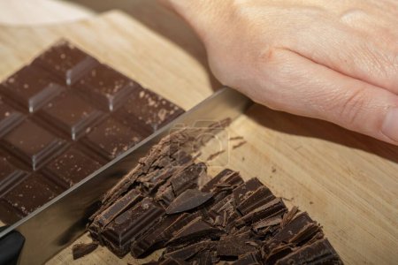 Photo for A closeup of a chef chopping chocolate bar into pieces with a knife on a cutting board - Royalty Free Image