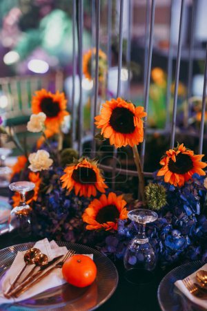 Foto de Una mesa vertical de un lugar con platos y utensilios rodeados de hermosas decoraciones florales, preparaciones para una celebración - Imagen libre de derechos