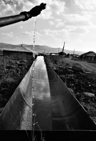 Téléchargez les photos : Une verticale d'eau coulant d'un tuyau dans un tube métallique dans un village tourné en niveaux de gris - en image libre de droit