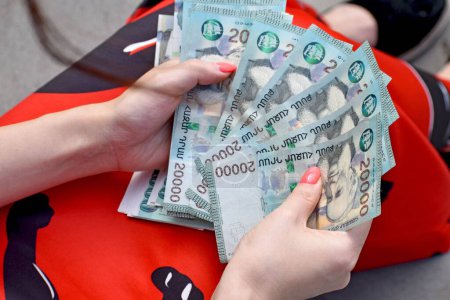 A top view of female hands in red dress holding and counting many Armenian 20000 dram bills