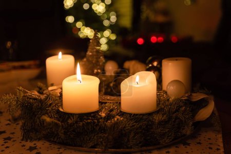 Foto de Un primer plano de cuatro velas encendidas en una mesa de madera, con un árbol de Navidad en el fondo - Imagen libre de derechos