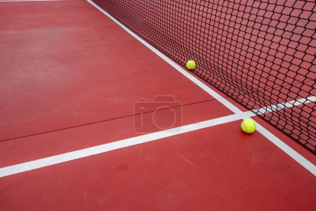 Téléchargez les photos : Les deux balles de tennis reposant au filet et les lignes de court sur un court en béton rouge - en image libre de droit