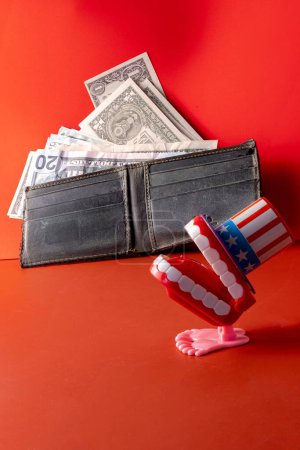 Foto de Una billetera con los billetes al lado de una decoración de dientes de temática estadounidense en una superficie roja - Imagen libre de derechos