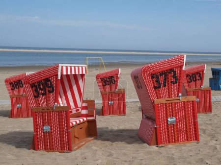 Foto de Sillas de playa con capucha roja, en la playa de la isla Langeoog, a lo largo de un camino de playa, con vistas al mar, en un día soleado - Imagen libre de derechos