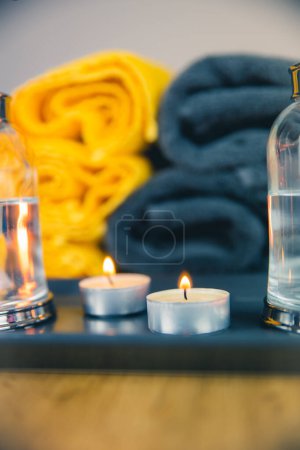 Photo for A vertical closeup shot of burning candles and liquids before gray and yellow towels - Royalty Free Image