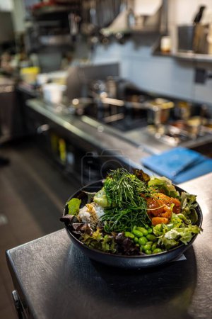 Photo for A vertical shot of a bowl of salad with healthy veggies on a wooden table in a kitchen - Royalty Free Image