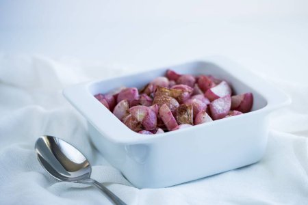 Photo for A closeup of the bowl of red sliced potatoes near the silver spoon on a white fabric during the daytime - Royalty Free Image