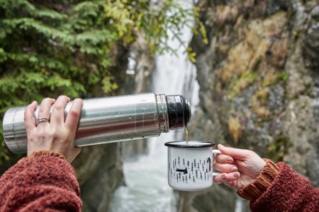 Foto de Una vista panorámica de una mujer que vierte café en una taza mientras admira la cascada Tatzelwurm - Imagen libre de derechos