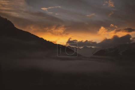 Foto de Una vista impresionante del oscuro paisaje nublado al atardecer con niebla en la montaña en primer plano - Imagen libre de derechos