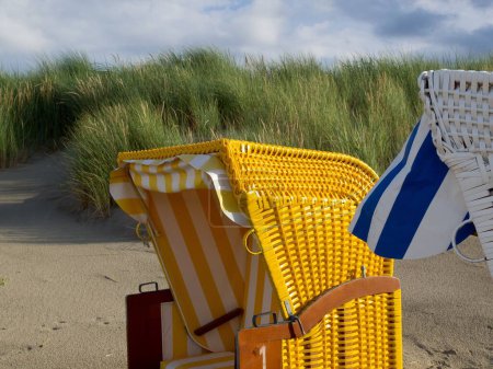 Téléchargez les photos : Un gros plan de chaises de plage à capuchon, sur la plage de sable de l'île Juist en mer du Nord, par une journée nuageuse, avec de l'herbe verte en arrière-plan - en image libre de droit