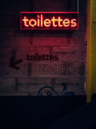 Photo for A vertical shot of a neon toilet sign hanging on the wall along a graffiti text in Nantes, France - Royalty Free Image
