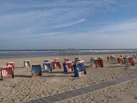 Téléchargez les photos : Chaises de plage à capuchon colorées, sur la plage de sable de l'île Langeoog en mer du Nord, par une journée nuageuse avec vue sur la mer en arrière-plan - en image libre de droit