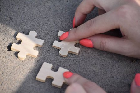 Téléchargez les photos : Une vue de dessus des mains féminines reliant deux pièces de puzzle en bois sur le sol - en image libre de droit