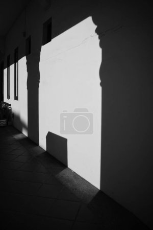 Téléchargez les photos : Plan vertical en niveaux de gris d'un mur le long d'un trottoir, avec l'ombre de piliers dessus au coucher du soleil - en image libre de droit