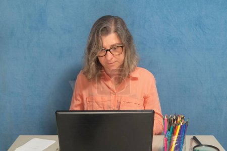 Téléchargez les photos : Une femme avec ordinateur portable travaillant à la maison ou au bureau - en image libre de droit