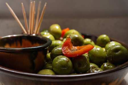 Photo for A closeup of a bowl of aceitunas, green olives and cut peppers shining from having an oily surface - Royalty Free Image