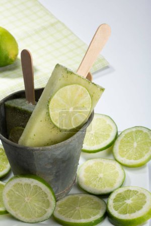 Photo for A vertical shot of lime flavor popsicles in a metal container decorated with sliced limes - Royalty Free Image