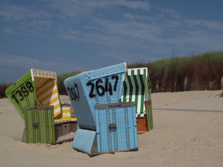 Foto de Coloridas sillas de playa con capucha, en la playa de Langeoog isla en el Mar del Norte, en un día nublado, con un camino de playa, y hierba verde en el fondo - Imagen libre de derechos