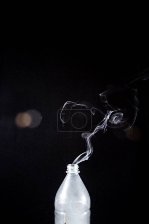 Téléchargez les photos : La fumée qui sort d'une bouteille en plastique sur fond noir - concept d'aromathérapie - en image libre de droit