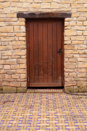 Photo for A vertical shot of a wooden door and brick walls in front of colorful paving stones of a street - Royalty Free Image