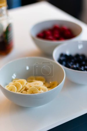 Photo for A vertical shot of three bowls with fresh bananas and other berries on a table - Royalty Free Image
