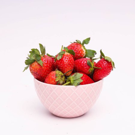 Téléchargez les photos : Gros plan d'un bol rose rempli de fraises devant un fond blanc - en image libre de droit