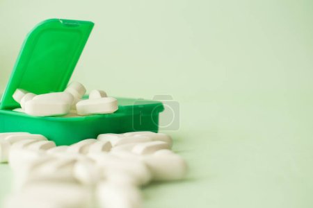 Foto de Un primer plano de píldoras blancas en un pillbox verde sobre un fondo blanco - Imagen libre de derechos