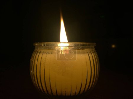 Foto de Un primer plano de una vela blanca ardiendo en un frasco transparente que ilumina el ambiente oscuro - Imagen libre de derechos