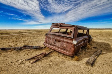 Foto de Un coche viejo destrozado metálico en medio de un campo seco y desolado bajo el cielo azul - Imagen libre de derechos