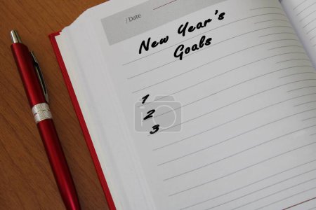 Photo for A closeup shot of a notepad with a pen on a wooden table for New Year's goals - Royalty Free Image