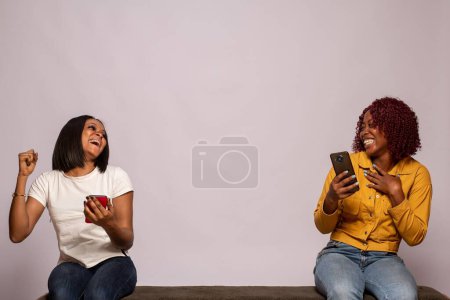 Foto de Chicas negras felices revisando sus teléfonos sintiéndose emocionados - Imagen libre de derechos