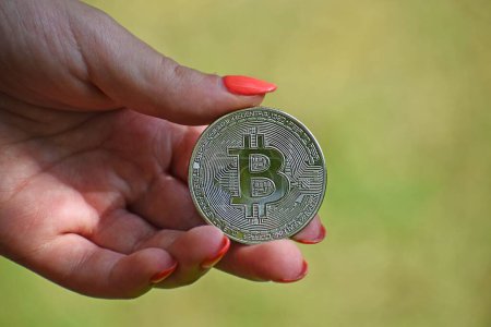 Foto de La mano de una mujer sosteniendo un bitcoin de plata sobre un fondo borroso - concepto de criptomoneda - Imagen libre de derechos