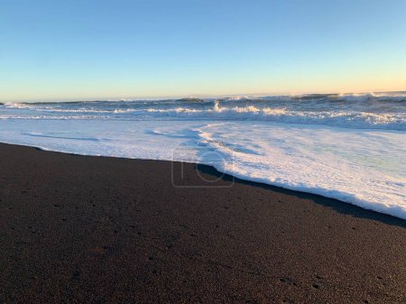 Foto de Las olas espumosas rompiendo la playa de arena Reynisfjara bajo el pintoresco atardecer en Islandia - Imagen libre de derechos