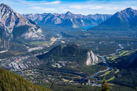 Photo for An illuminated cityscape in a grassy valley and a river, with a grassy hill in the middle, and rocky Sulphur Mountain in Canada in the background - Royalty Free Image