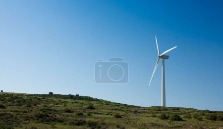 Téléchargez les photos : Une éolienne sur une colline avec un fond bleu ciel - en image libre de droit
