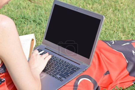 Téléchargez les photos : Un gros plan d'une femme assise sur l'herbe travaillant avec un stylo, un ordinateur portable et un ordinateur portable - en image libre de droit