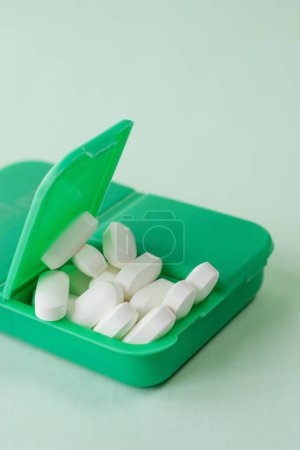 Foto de Un primer plano vertical de pastillas blancas en un pillbox verde sobre un fondo blanco - Imagen libre de derechos