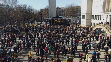Téléchargez les photos : Une vue par drone des gens qui se rassemblent devant une scène pour un événement avec drapeaux pendant la journée à Kaunas, Lituanie - en image libre de droit