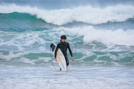 Téléchargez les photos : Un homme caucasien revenant de surf dans l'océan - en image libre de droit