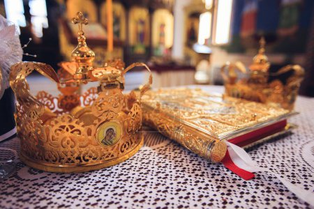 Téléchargez les photos : Gros plan d'une couronne d'or avec l'icône de Marie et du Christ dessus et une Bible sur une table - en image libre de droit