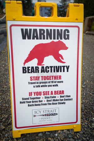 Téléchargez les photos : Un panneau d'avertissement vertical pour les touristes à Icy Straight Point pour se méfier des ours et rester ensemble en groupes tout en visitant - en image libre de droit