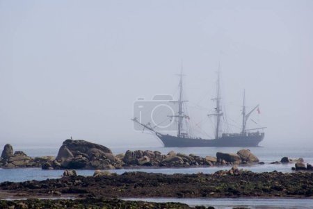 Téléchargez les photos : Une belle vue d'un grand bateau naviguant dans l'océan dans une brume près de la barrière de pierres - en image libre de droit