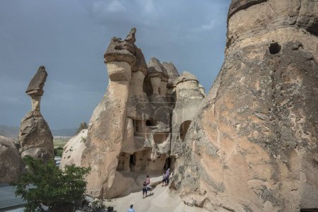 Téléchargez les photos : Un groupe de personnes, debout devant de belles formations de pierre dans la vallée du Pasabag en Cappadoce, avec un ciel orageux en arrière-plan - en image libre de droit