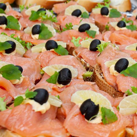 Téléchargez les photos : Un gros plan des canapés avec du saumon décoré d'olives noires et de citron - en image libre de droit