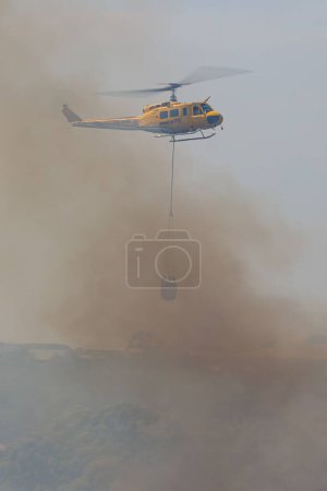 Photo for A vertical shot of a firefighting helicopter extinguishes a fire - Royalty Free Image