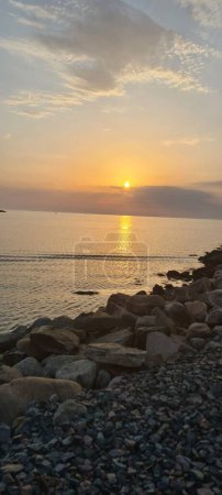 Téléchargez les photos : Vue panoramique verticale du coucher de soleil depuis une côte sablonneuse d'un océan - en image libre de droit